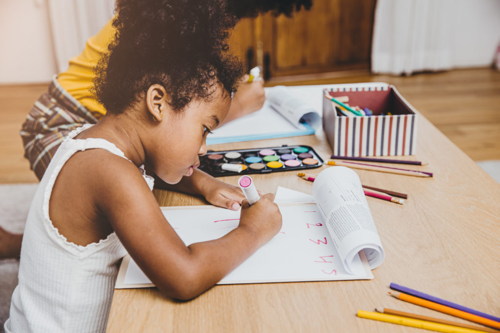 American Black preschool daughter kids doing homework learning education with her sister living together at home.