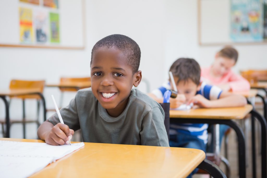 Disabled pupil writing at desk in classroom