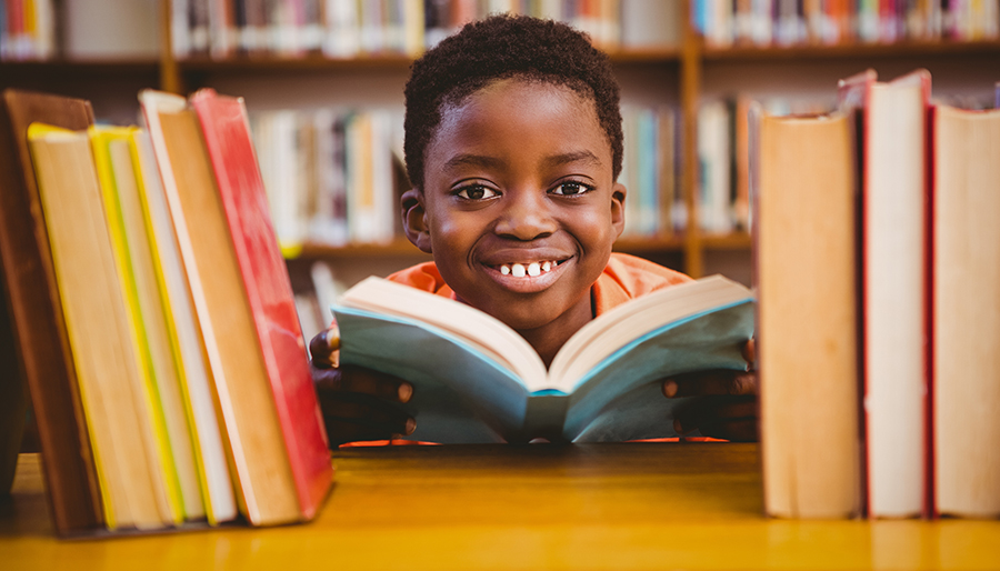 Cute african american boy reading book in library