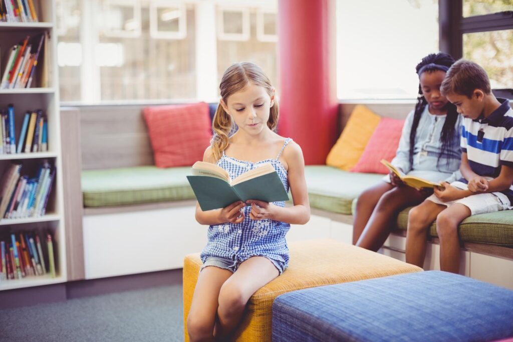 School kids sitting on sofa and reading book in library