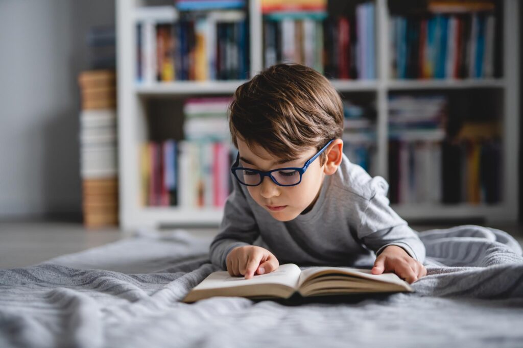One caucasian boy lying on the floor at home in day reading a bo