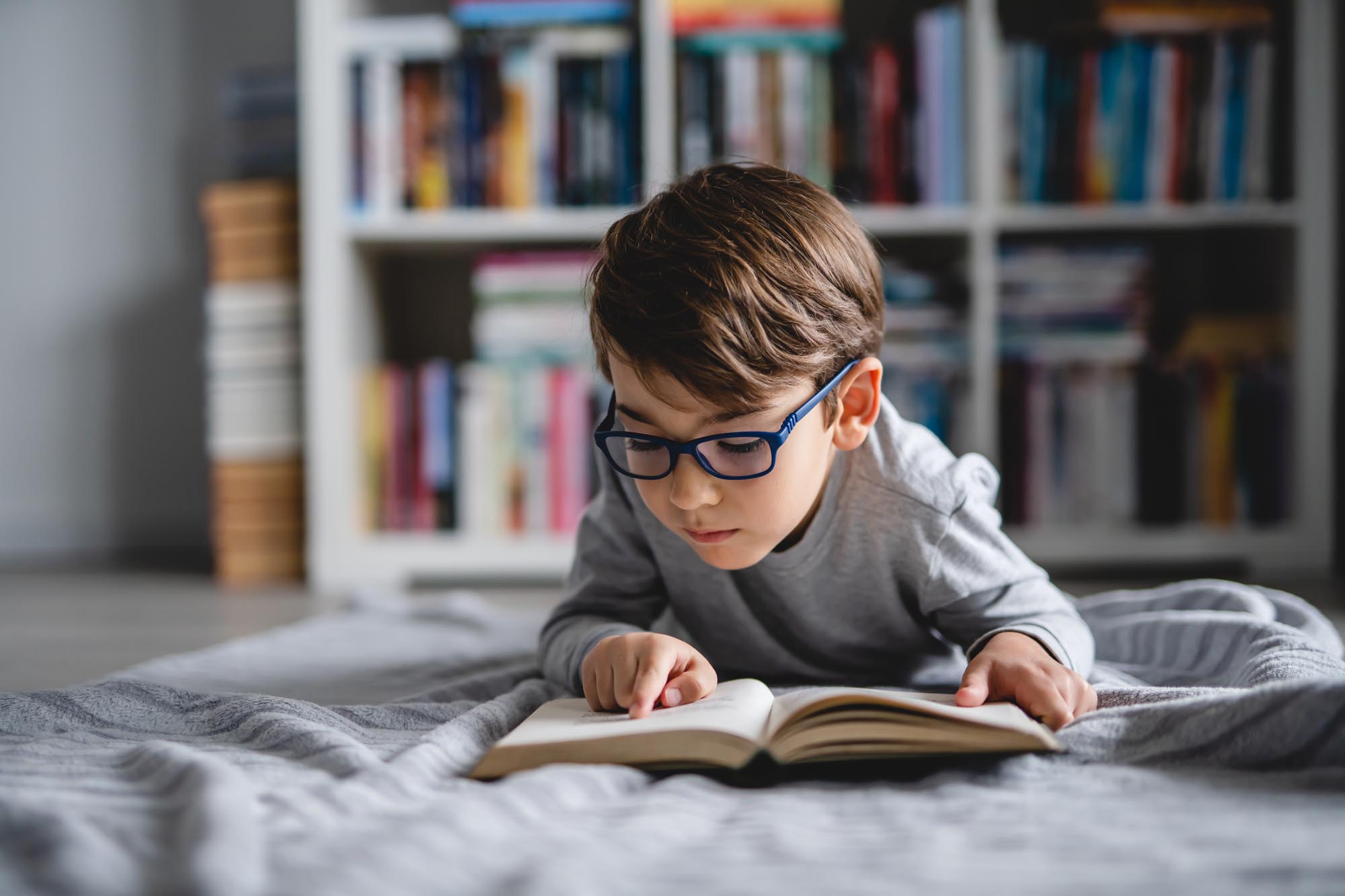 One caucasian boy lying on the floor at home in day reading a bo