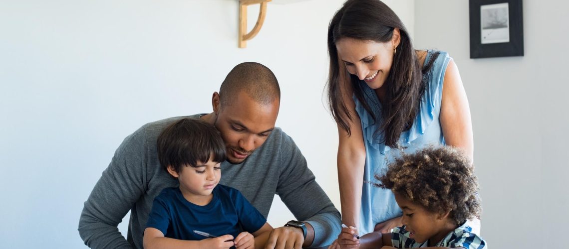 Multiethnic parents helping children with their homework at home. Young father and mother helping sons study at living room. Little boys completing their exercises with the help of dad and mom.