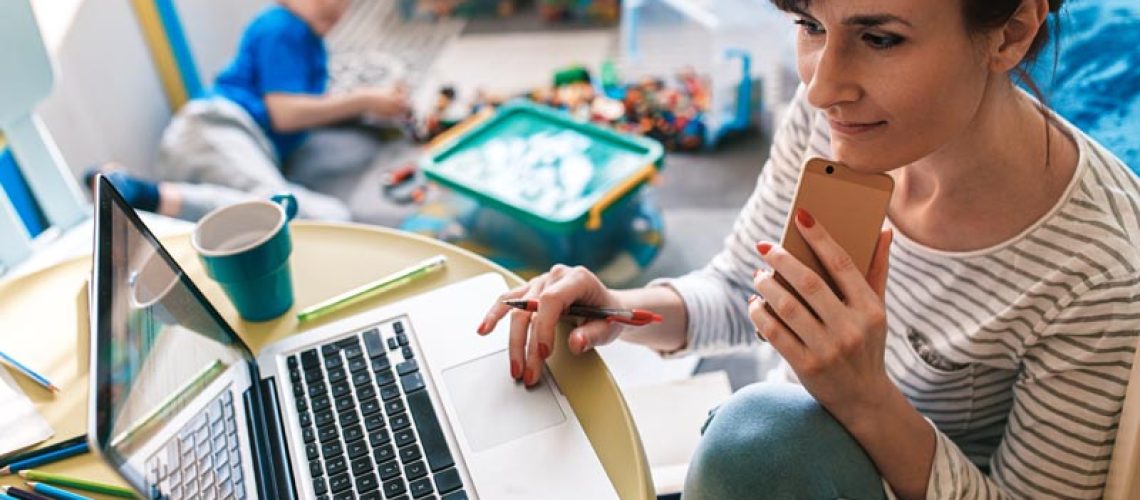 Mother working remotely on laptop while taking care of her son p