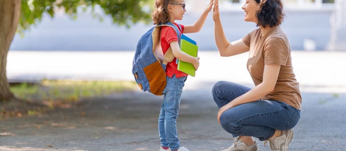 Parent and pupil of primary school go hand in hand. Woman and girl with backpack behind the back. Beginning of lessons. First day of fall.