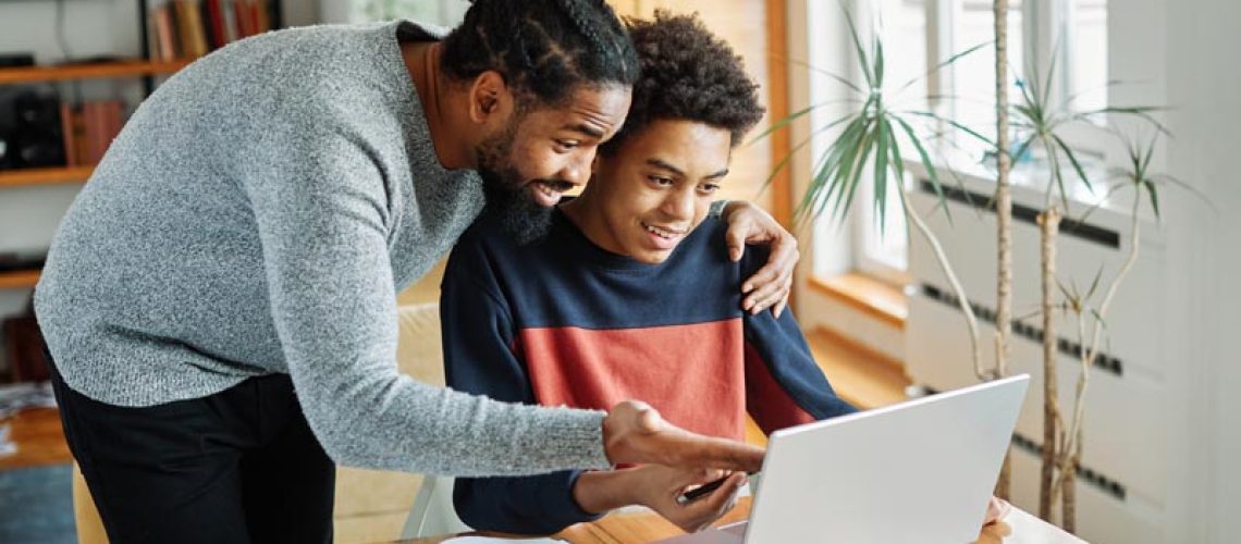 Father and son doing homework with laptop at home. Father and teenage son using laptop. Boy and dad sitting at home working with notebook