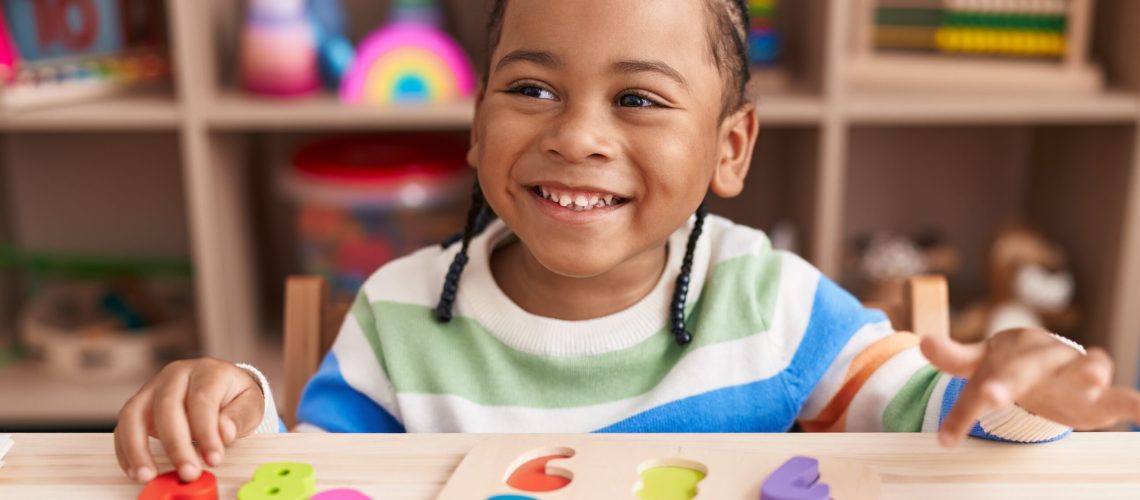 African american boy playing with maths puzzle game sitting on table at kindergarten